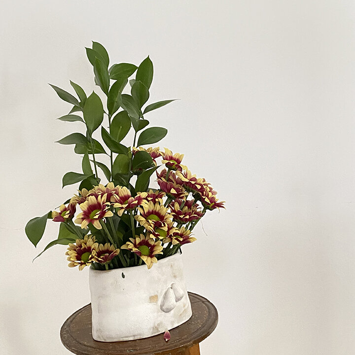 Vertical floral design. small white vase, yellow and brown flowers, green branches are taller