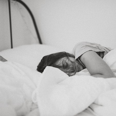 woman sleeping, black and white photo, only her face an arm is visible and part of bed