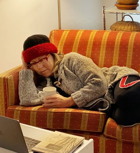 woman watching something on computer, she is on a sofa and is wearing a hat
