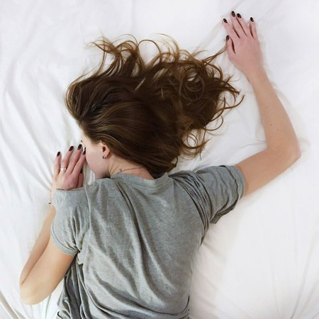 woman wearing a grey t shirt, sleeping with her tummy down, hair spread out