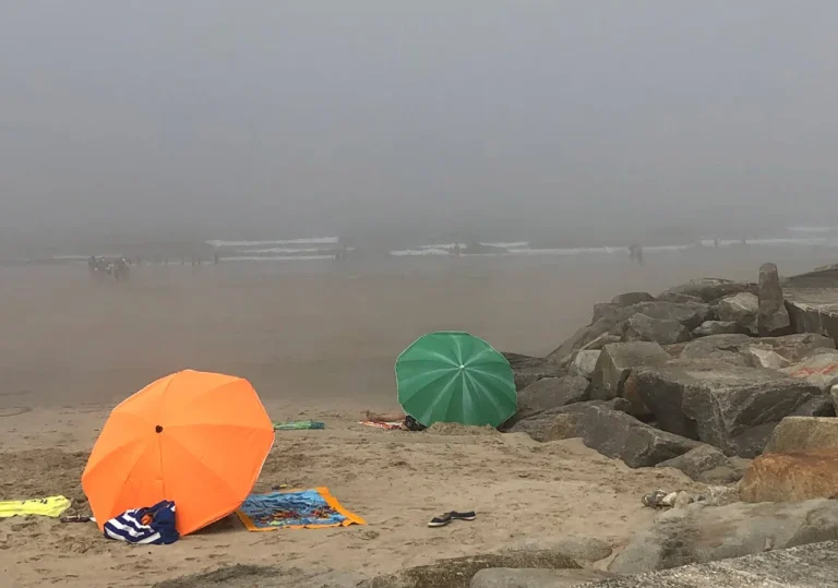 Foggy day at the Matosinhos Beach, Orange sunbrella in the foreground, green sunbrella in the background, rocks on right side