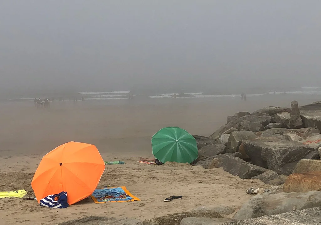 Foggy day at the Matosinhos Beach, Orange sunbrella in the foreground, green sunbrella in the background, rocks on right side