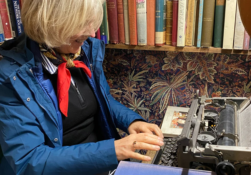 Woman wearing a blue jacket and a red scarf writing on a typewriter