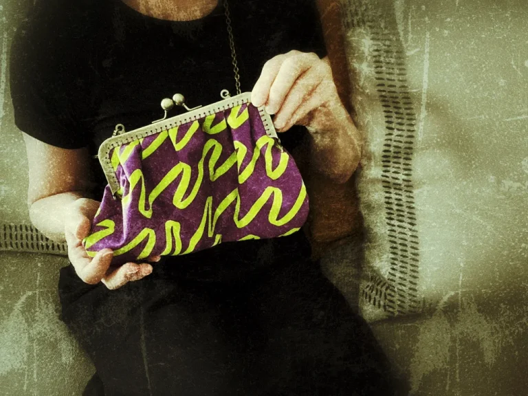part of a body wearing all black and hand holding a purble and green handbag