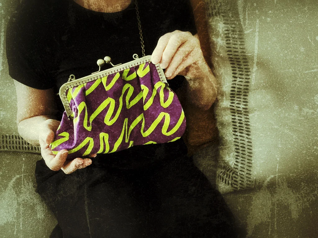 part of a body wearing all black and hand holding a purble and green handbag