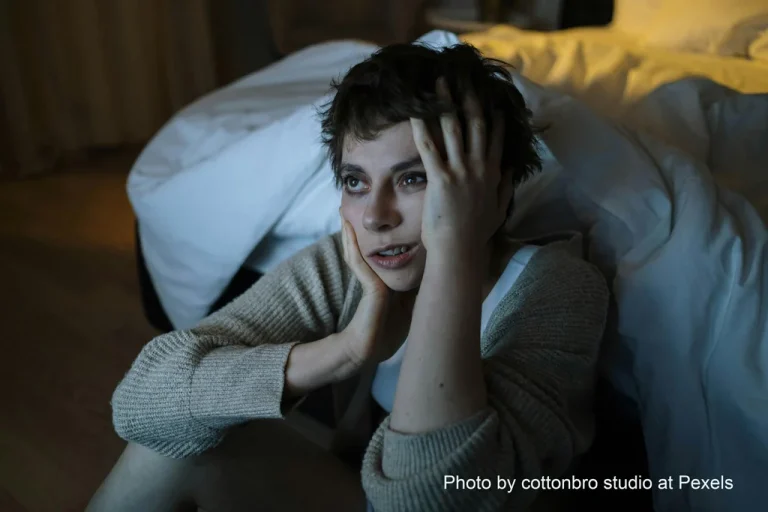 photo of woman on floor next to bed wide awake, sleepless nights