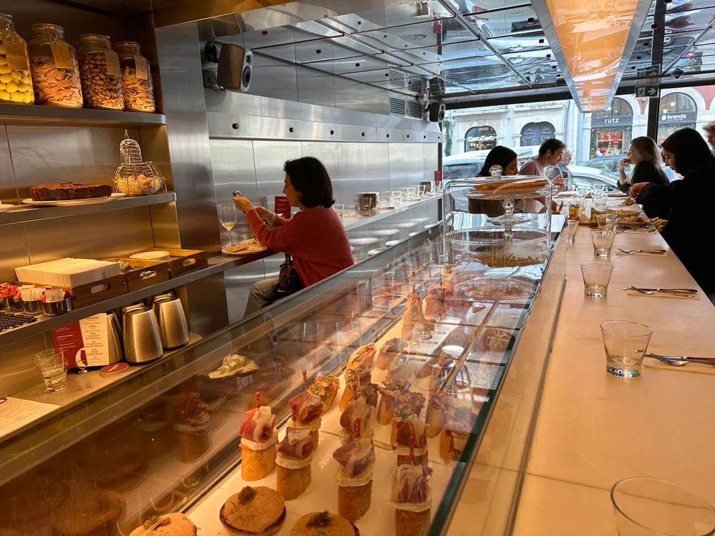 counter at a tapas restaurant, tapas in a glass counter top, metal walls, people in the background