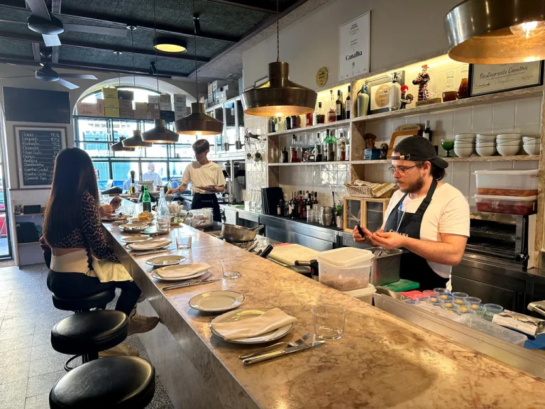 Counter seating with dishes on counter, chef working, large window at end of counter, canalha restaurant