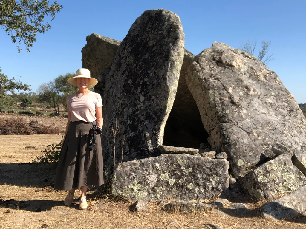 Woman in front of megalithic stones, she is wearing a hat, a pink t shirt, skirt and holding a camera. Marvão