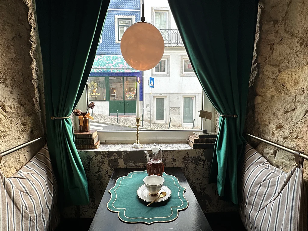 Tea and tea cup on a table, bench on either side, window with view of Lisbon street, cozy ideas