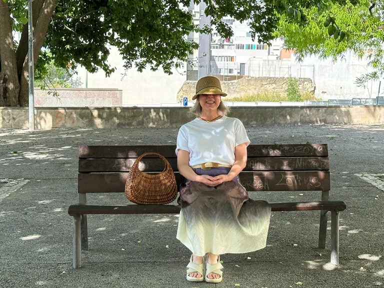 woman siting on bench, hat over face, straw bag next to her, where to sit in Lisbon